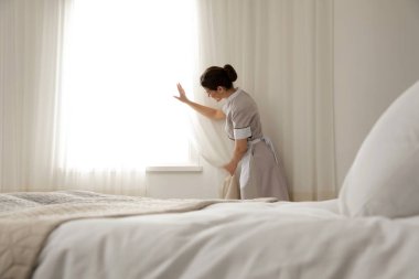 Otel odasında perdeleri açan genç hizmetçi.