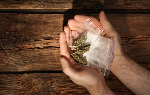 Man holding plastic bags with cocaine and hemp buds on wooden background, top view. Space for text — Stock Photo, Image