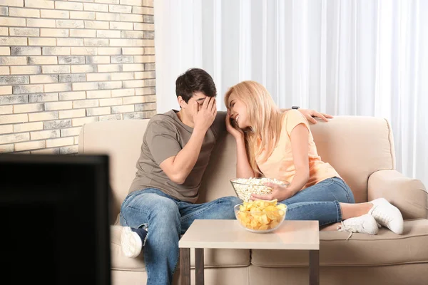 Jovem casal com lanches assistindo TV no sofá em casa — Fotografia de Stock