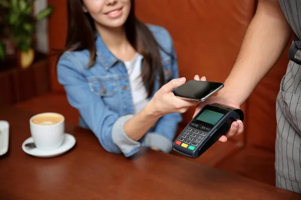 Woman using terminal for contactless payment with smartphone in cafe, closeup — Stock Photo, Image