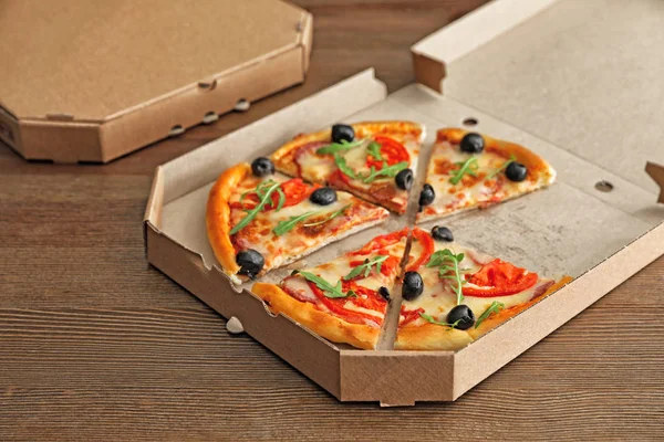 Cardboard box with tasty pizza on wooden background