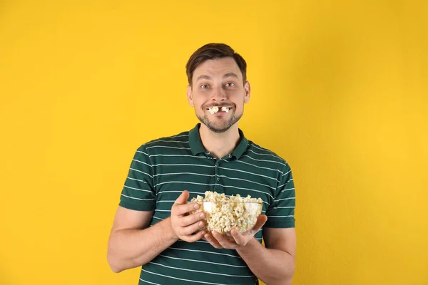 Hombre comiendo palomitas sabrosas sobre fondo de color — Foto de Stock