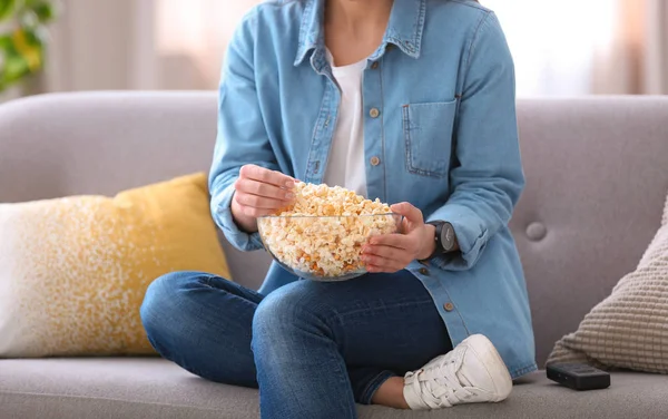 Young woman watching movie with popcorn in living room, closeup