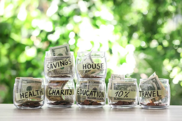 Pots en verre avec de l'argent pour différents besoins sur la table sur fond flou — Photo