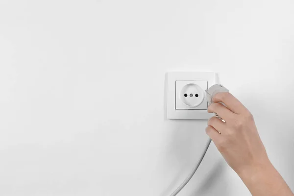 Woman putting plug into power socket on white background, closeup. Electrician\'s equipment