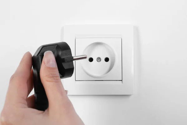 Woman putting plug into power socket on white background, closeup. Electrician's equipment — Stock Photo, Image