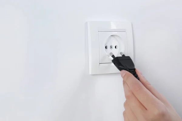 Mujer poniendo enchufe en toma de corriente sobre fondo blanco, primer plano. Equipos de electricista — Foto de Stock