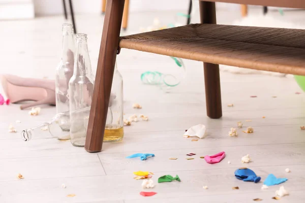 Suelo desordenado con botellas vacías cerca de la mesa. Después del caos fiesta —  Fotos de Stock