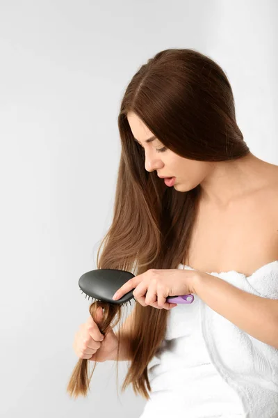 Woman struggles to brush her hair on light background — Stock Photo, Image