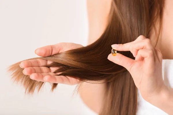 Mujer sosteniendo cápsula vitamínica para la salud del cabello sobre fondo claro, primer plano — Foto de Stock