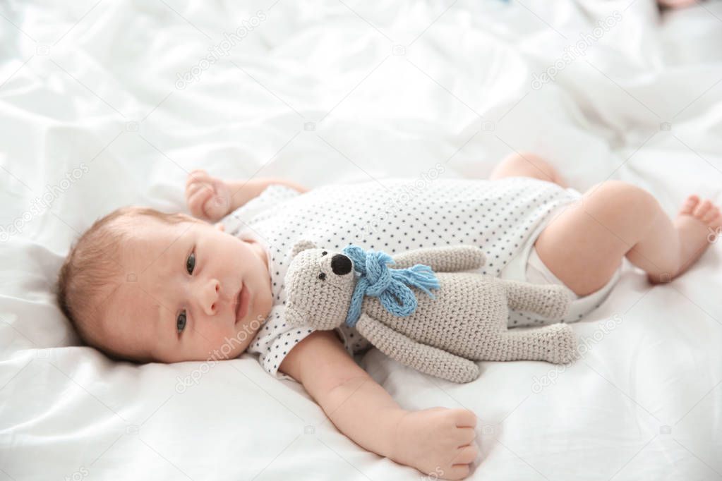 Adorable newborn baby with toy lying on bed sheet