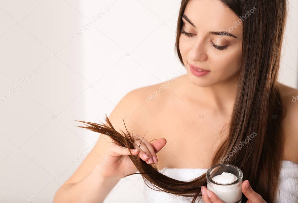 Woman with glass bowl of hair mask on light background. Space for text