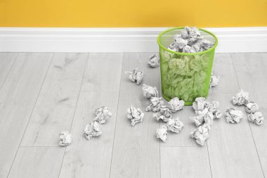 Metal bin with crumpled paper on floor near color wall, space for text clipart