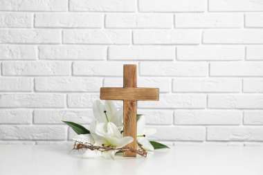 Tahta haç, taç dikenler ve duvara karşı masada lilyum çiçeği