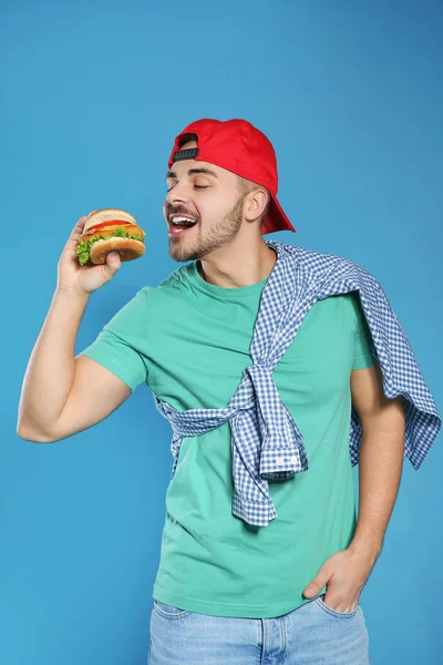 Bello uomo mangiare gustoso hamburger su sfondo di colore — Foto Stock