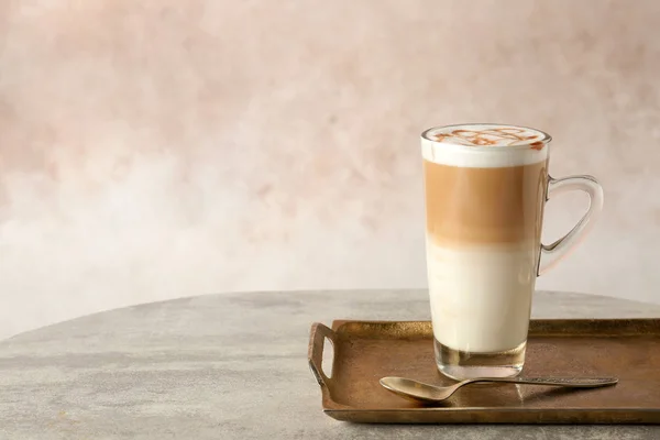 Tray with glass cup of caramel macchiato and syrup on table against color background. Space for text — Stock Photo, Image