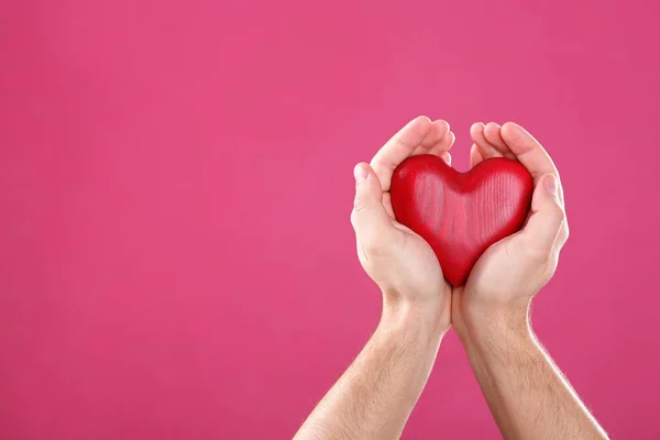 Hombre sosteniendo el corazón decorativo en las manos sobre el fondo de color, espacio para el texto — Foto de Stock