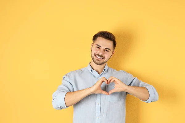 Retrato del joven haciendo corazón con las manos en el fondo de color — Foto de Stock