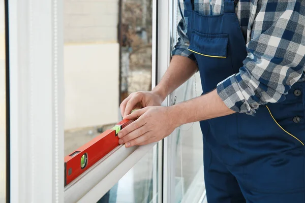 Trabalhador da construção usando o nível da bolha ao instalar a janela dentro de casa, close-up — Fotografia de Stock