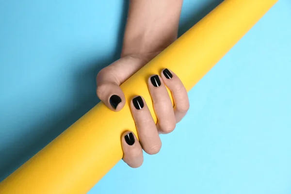 Woman with black manicure holding paper roll on color background, closeup. Nail polish trends