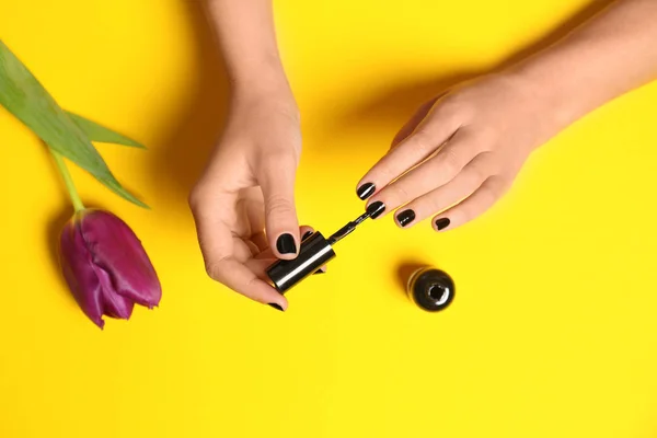 Mujer aplicando esmalte de uñas en flor sobre fondo de color, primer plano — Foto de Stock