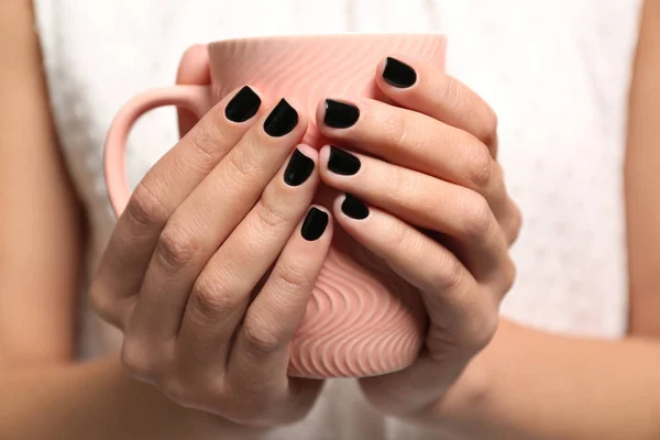 Woman with black manicure holding cup, closeup. Nail polish trends