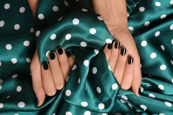 Woman with black manicure holding color fabric, top view. Nail polish trends