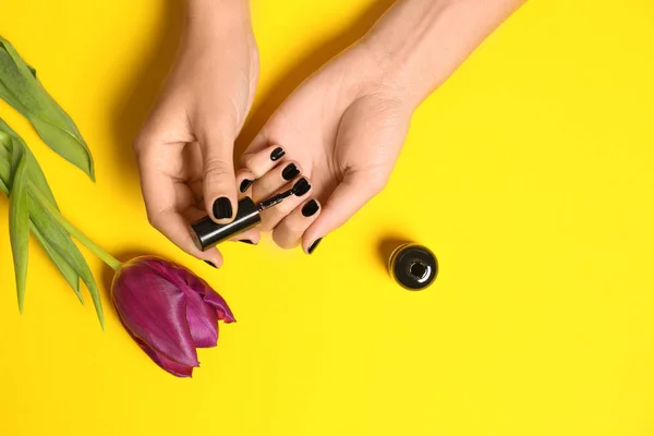 Mujer aplicando esmalte de uñas en flor sobre fondo de color, primer plano — Foto de Stock