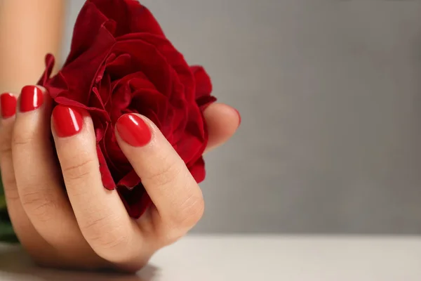 Mujer con manicura roja sosteniendo rosa sobre fondo borroso, primer plano. Tendencias de esmalte de uñas — Foto de Stock