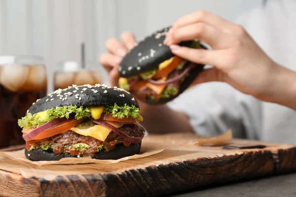 Tasty burger with black buns and woman eating on background