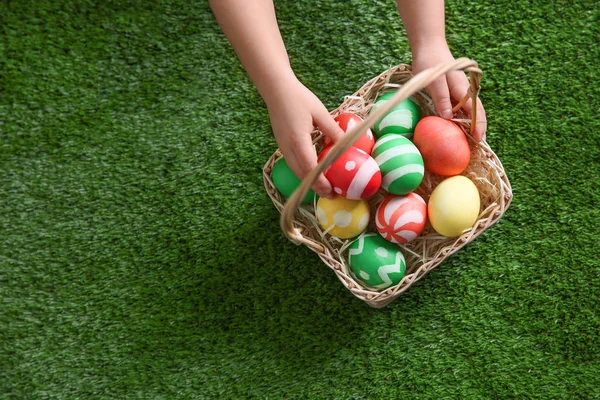 Niño pequeño con cesta de huevos de Pascua pintados sobre hierba verde, vista superior. Espacio para texto — Foto de Stock