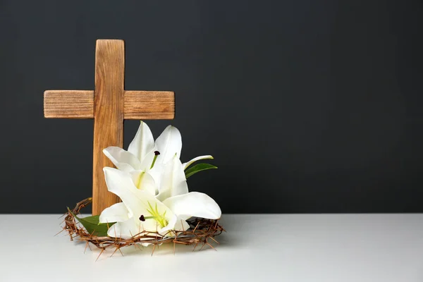 Houten kruis, kroon van doornen en bloesem lelies op tafel tegen een achtergrond met kleur, ruimte voor tekst — Stockfoto