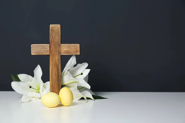 Houten kruis, paaseieren en bloesem lelies op tafel tegen een achtergrond met kleur, ruimte voor tekst — Stockfoto