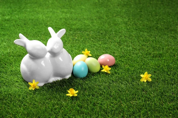 Ceramic Easter bunnies and dyed eggs on green grass, space for text — Stock Photo, Image