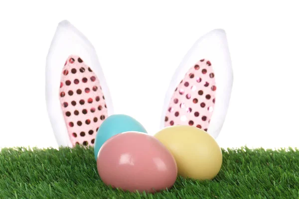 Dekoracyjne Easter bunny uszy i barwione jaja na zielonej trawie na białym tle — Zdjęcie stockowe