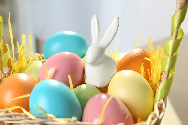 可爱的陶瓷复活节兔子和染色鸡蛋在柳条篮在桌子上, 特写镜头 — 图库照片