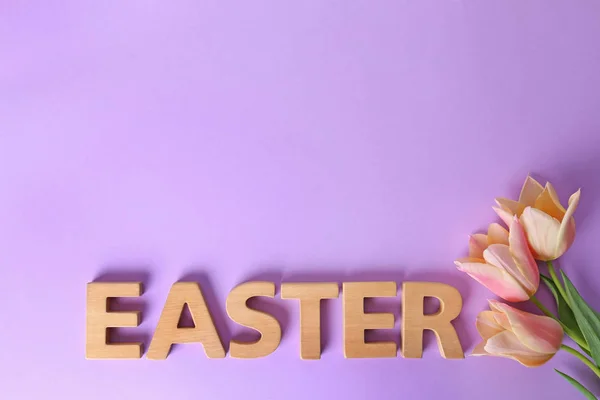 Frühlingsblumen und Wort Ostern aus Holzbuchstaben auf farbigem Hintergrund, Draufsicht. Raum für Text — Stockfoto