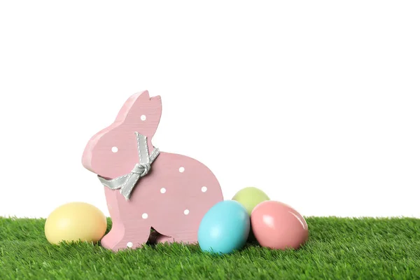 Cute wooden Easter bunny and dyed eggs on green grass against white background, space for text — Stock Photo, Image