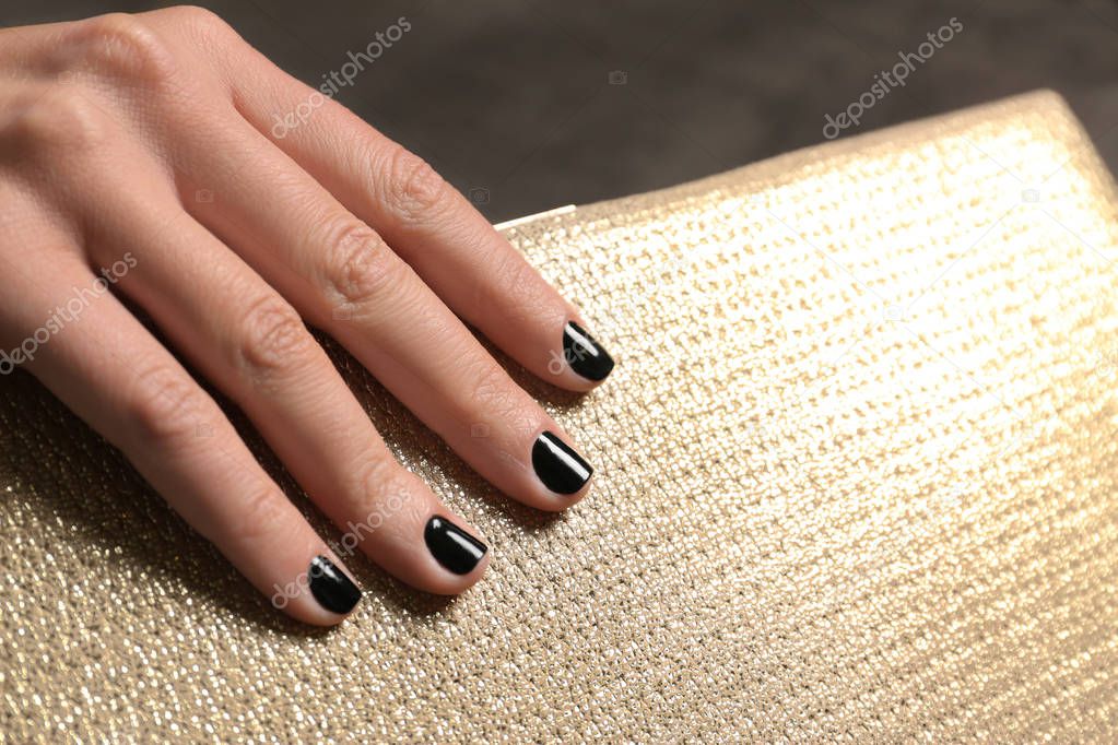 Woman with black manicure holding clutch, closeup. Nail polish trends