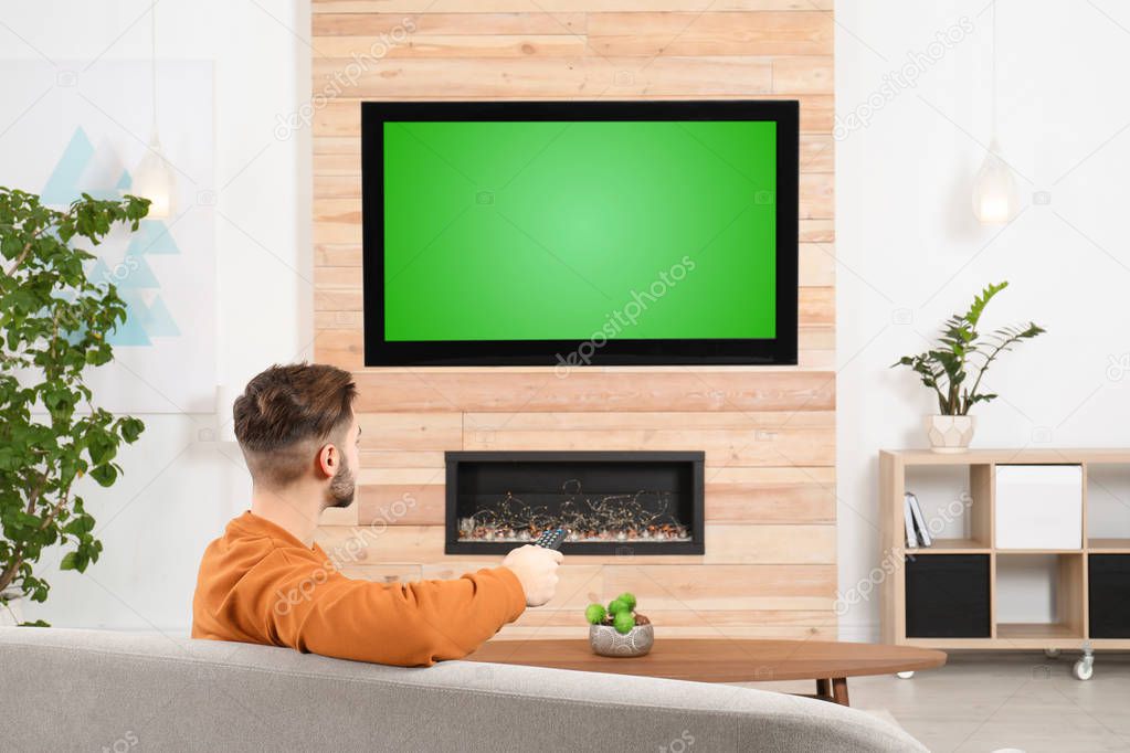Man watching TV on sofa in living room with decorative fireplace