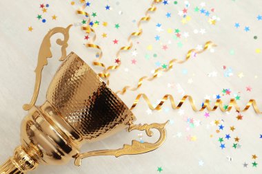 Golden trophy cup with streamers on wooden background. Space for text clipart