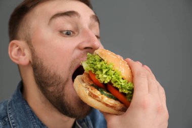 Genç adam gri arka plan üzerinde lezzetli hamburger yeme