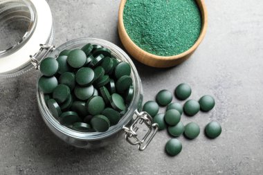 Cam Kavanoz yeşil spirulina hapları ve toz kase gri tablo ile düz yatıyordu bileşimi