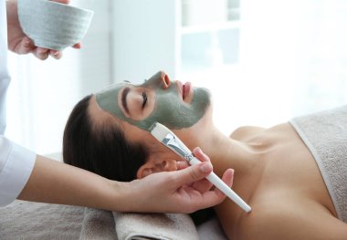 Spa salonu müşterinin yüzüne maske uygulayarak güzellik uzmanı