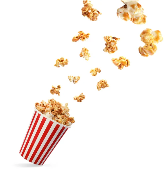 Delicious caramel popcorn falling into carton cup on white background — Stock Photo, Image