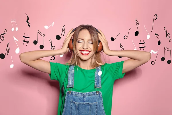 Wanita muda bergaya yang mendengarkan musik dengan headphone dan catatan terbang dengan latar belakang warna — Stok Foto