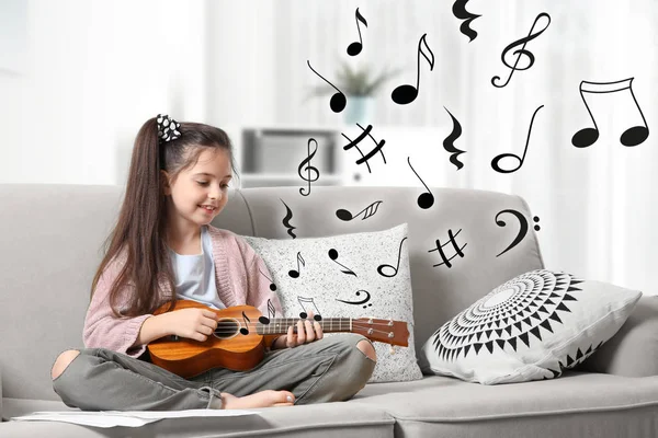 Menina bonito tocando guitarra no sofá e voando notas de música no quarto — Fotografia de Stock