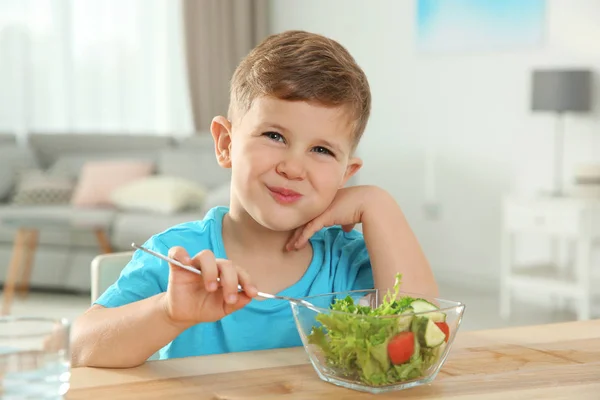 Adorable little boy eating vegetable salad at table in room — Stock Photo, Image