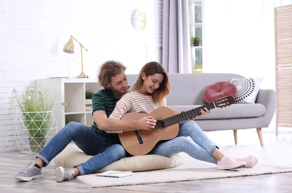 Joven enseñando a su novia a tocar la guitarra acústica en la sala de estar — Foto de Stock