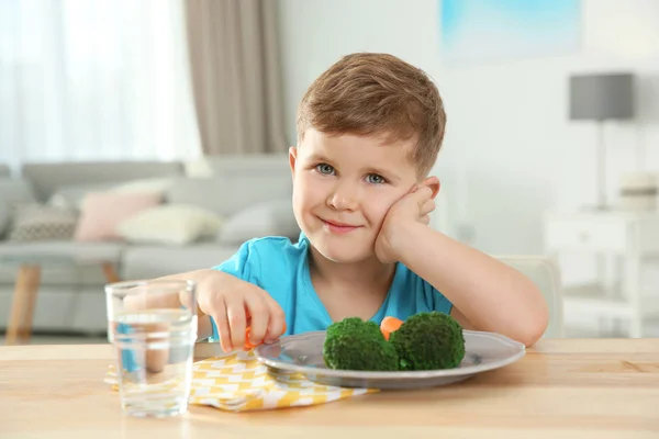 Adorable little boy with plate of vegetables at table in living room — Stock Photo, Image